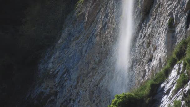Солнце светит на водопад рядом со скалой — стоковое видео