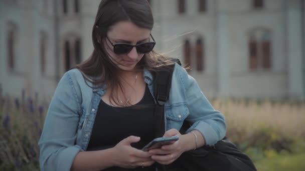 Una Mujer Chaqueta Mezclilla Con Una Mochila Sosteniendo Teléfono Mientras — Vídeos de Stock