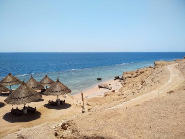 Yazın sahil ve deniz. Sahilde kum tepeleri ve şemsiyeler.