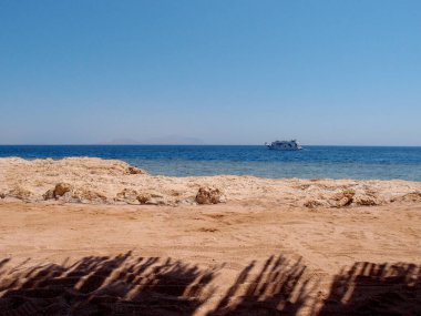 Beach with sand and rocks, sea, waves and pleasure boat