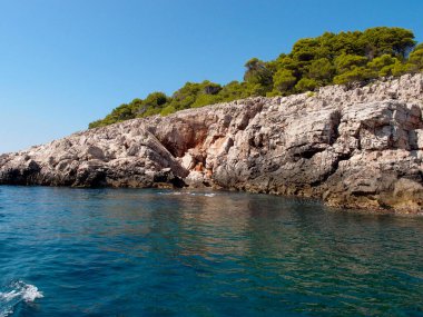 Beautiful view of the rocky coast of the island with a forest and blue sky in the background, a view from the sea