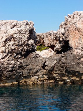 Adanın kayalık kıyılarının güzel manzarası. Arkasında orman ve mavi gökyüzü var. Denizden bir manzara.