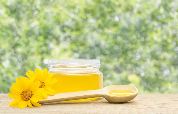 a jar of honey and a spoon with honey next to it on a green defocused background
