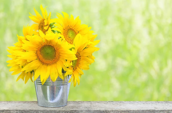 A bouquet of sunflower flowers in a metal vase on a wooden bar with copy space