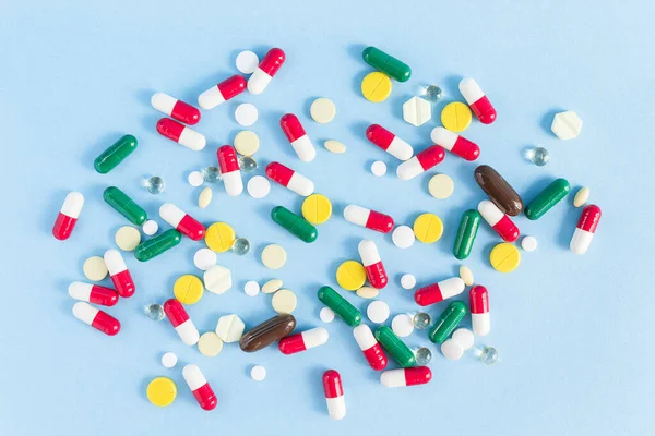 Pills of different shapes and colors are scattered on a blue background
