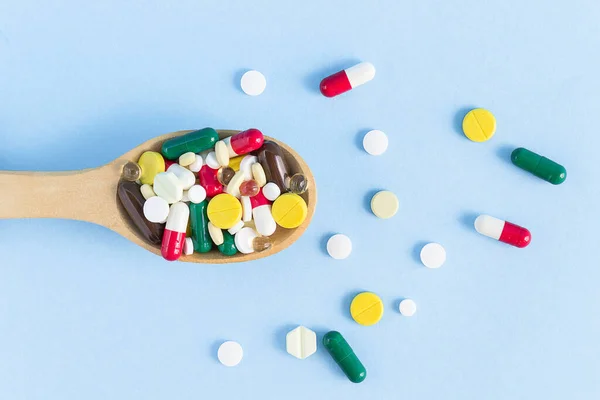 Top view of a wooden spoon filled with various pills on a blue background