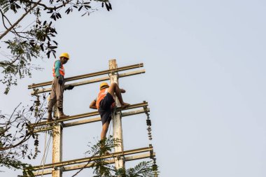 30 Aralık 2021, Baraipur, Batı Bengal, Hindistan: Yolun kenarına elektrik direği kuran ve alüminyum kabloya bağlanan iki işçi.