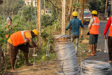 30 Aralık 2021, Baraipur, Batı Bengal, Hindistan: Yolun kenarına elektrik direği kuran ve alüminyum kabloya bağlanan iki işçi.