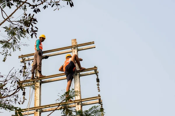 30 Aralık 2021, Baraipur, Batı Bengal, Hindistan: Yolun kenarına elektrik direği kuran ve alüminyum kabloya bağlanan iki işçi.