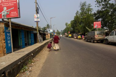 12 Aralık 2021, Narendrapur, Batı Bengal, Hindistan: Yaşlı bir adamın çantasını taşımasına yardım etmeye çalışan küçük bir kız. Seçici odak.