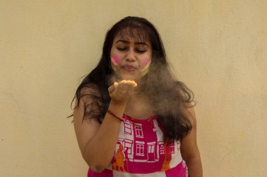 Holi pudra renkleriyle oynayan genç ve güzel bir Hintli bayan. Sarı arkaplan ile seçmeli odak.