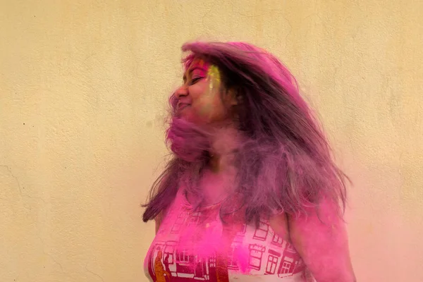 Holi pudra renkleriyle oynayan genç ve güzel bir Hintli bayan. Hareket bulanıklığı efektli seçici odak ve sarı arkaplan.