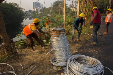 30 Aralık 2021, Baraipur, Batı Bengal, Hindistan: Yolun kenarına elektrik direği kuran ve alüminyum kabloya bağlanan iki işçi.