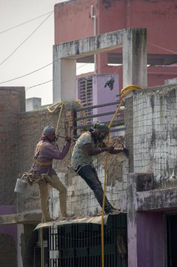 9 Şubat 2022, Kolkata, Batı Bengal, Hindistan: İple asılarak dış duvarın onarımını yapan iki inşaat işçisi. Seçici odak.