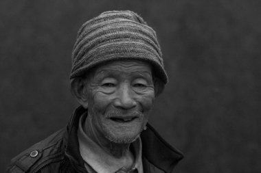 Black and white photo of an Nepali old man laughing with lots of wrinkle on his face, selective focus.