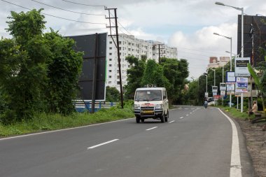 10 Temmuz 2022, Narendrapur, Batı Bengal, Hindistan: Yol kenarındaki ağaçlarla dolu güzel bir yol ve hareket halindeki bir ambulans az hareket bulanıklığı etkisi.