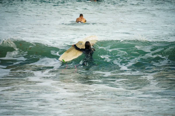 在加那利群岛的兰萨罗特岛 身穿黑色湿衣的年轻人和他的董事会一起冲浪 — 图库照片