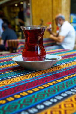 Small glass of Turkish red tea on a table with a colorful tablecloth