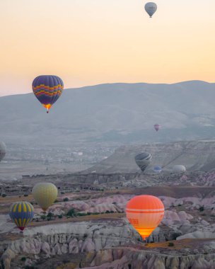 Güneşli bir yaz günü turistlerle Goreme şehrinin üzerinde uçarken balonlar yakıt yakıyor.