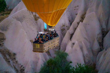 Güneşli bir yaz günü turistlerle Goreme şehrinin üzerinde uçarken balonlar yakıt yakıyor.