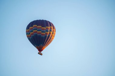 Colorful balloon flying over a clear blue sky with a basket for passenger transport during a sunset on a sunny day, copy space