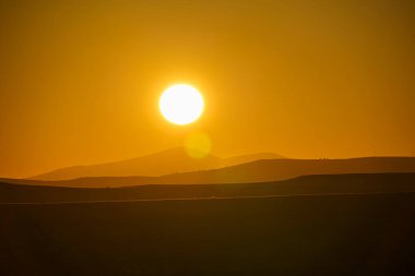 Bulutsuz bir günde, dağ oluşumlarının üzerinde turuncu renklerle gün batımı