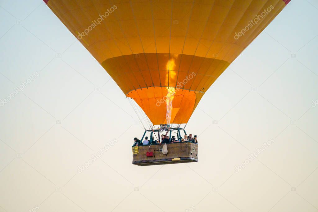 Balloons burning fuel as they fly over the city of Goreme with sightseeing tourists during a sunny summer day