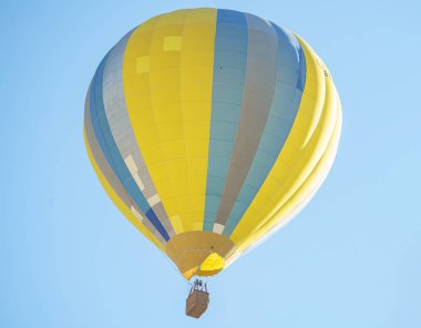 Yellow and blue balloon with a small basket flying over Cappadocia during a sunny day with a clear blue sky