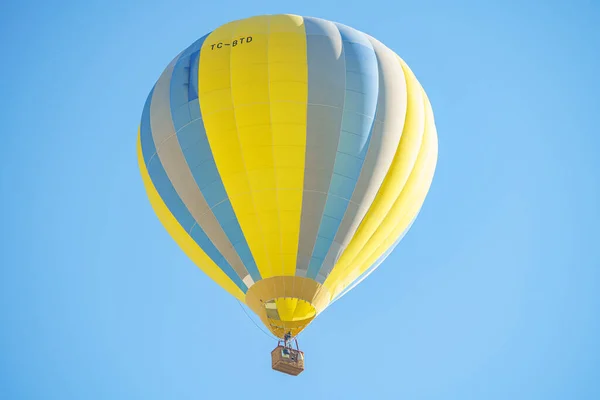 Açık mavi gökyüzü ile güneşli bir günde Kapadokya üzerinde uçan küçük bir sepet ile sarı ve mavi balon