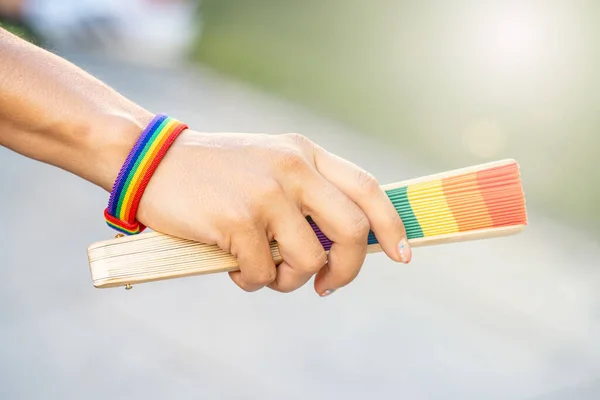 Woman holding a fan with the multicolored gay flag, a rainbow bracelet and multi-colored fingernails, on the occasion of gay and LGBTI pride during a sunny summer day