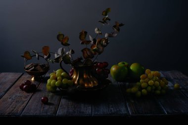 Fruit still life with grapes, apples, chocolate and antique copper utensils on dark wooden table background