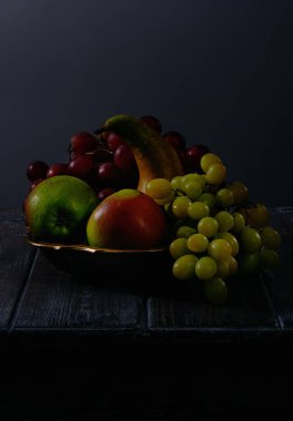Fruit still life with grapes, apples and pears in antique copper bowl on dark wooden table background