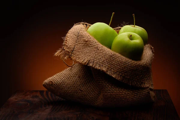 在深色木制桌子和温暖的乡村背景上的布袋中的有机绿色苹果 — 图库照片