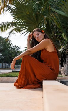 Terracotta elbiseli, kulağında çiçekle sokakta oturan güzel İspanyol kadın.