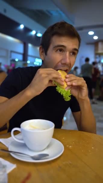 Hispanic young man eats a sandwich in a bar and says ok with his hand — Stock Video