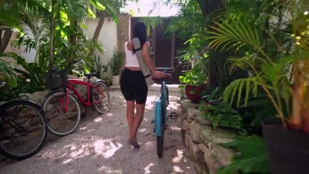 Молодая женщина хватает свой велосипед, чтобы выйти из дома с ковриком для йоги — стоковое видео