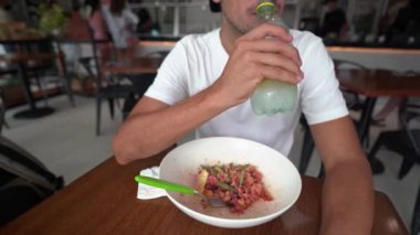 Genç İspanyol bir adam bir restoranda salata yerken soda içer.