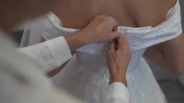 Gelinliğin düğmelerini ilikleyen nedimelerin yakın çekimi.