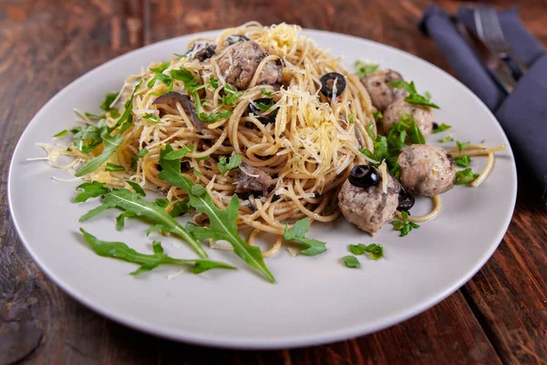 Spaghetti with meatballs, olives and arugula on wood table — Stock Photo, Image