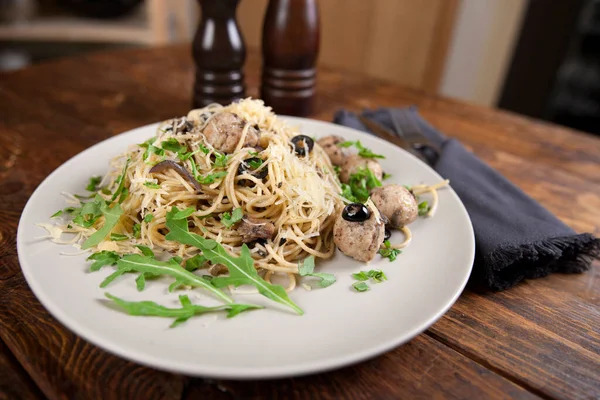 Spaghetti med köttbullar, oliver och ruccola på träbordet Stockbild