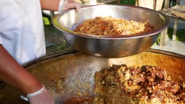Hef cook and put spanish paella on the plate with shrimp, meat, mussel, rice, spice, saffron in huge paella pan at food market. — Vídeo de Stock
