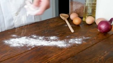 Fırıncının yakın çekimi mutfağa un döker. Başla. Fırıncı ahşap masaya bir tutam un serpti.