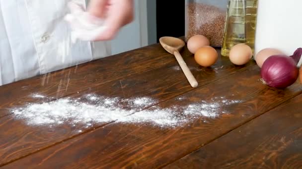 A pék közelről lisztet önt a konyhába. Felvétel. Baker megszórja csipetnyi liszt a fa asztalon — Stock videók