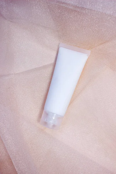 Mockup white plastic tube for moisturizer, lotion, facial cleanser or shampoo on smudged cream texture background top view. Delicate purity skin care product