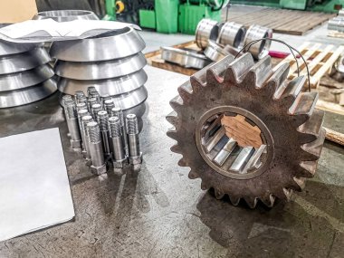 Depodaki masada bir dişli ve makineye yerleştirilmiş birkaç cıvata parçası var..