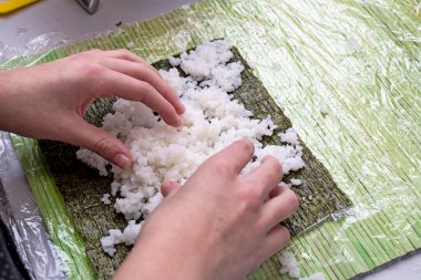 On a sheet of nori, a girl spreads rice for making sushi.