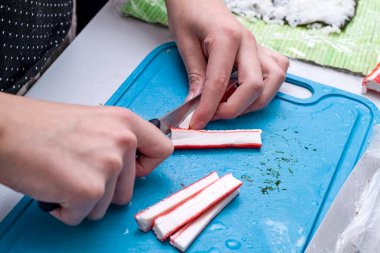 Girl cuts crab sushi on the kitchen board.