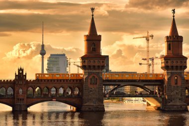 Berlin 'de gün batımına karşı nehri geçen bir trenle Eski Oberbaşemcke Köprüsü