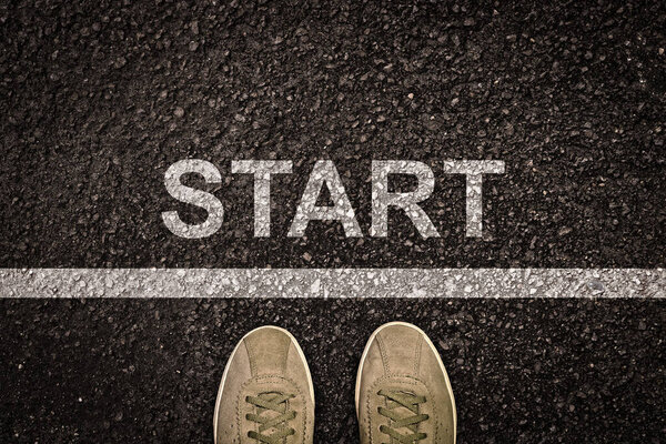 The inscription "Start" on the asphalt and feet in sneakers. View from above. Starting line. The concept of innovation and life success.