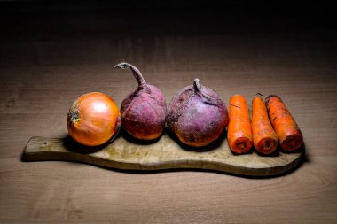 Tahta doğrama tahtasındaki çorba için çiğ sebze soğan, pancar, havuç. Vejetaryenlik ve sağlıklı gıda kavramı.